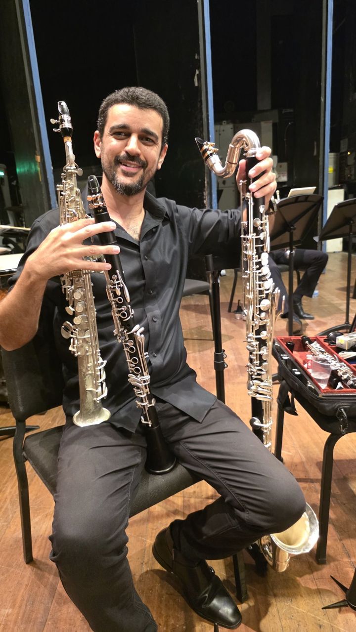 Nir Marom smiling backstage with a soprano saxophone, a clarinet and a bass clarinet