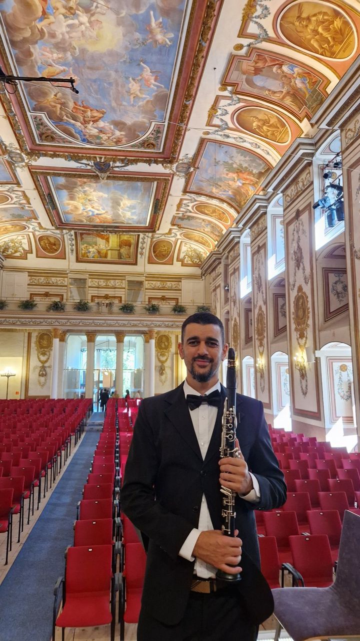 Nir Marom in concert dress, holding his clarinet in an ornate concert hall